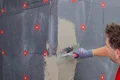 Heimwerker verputzt Dämmelemente einer Fassade mit einer glatten Spachtel, um eine gleichmäßige Oberfläche zu erzielen.