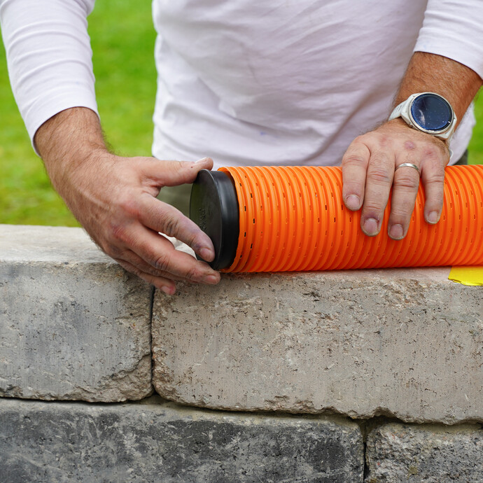Detailfoto: Verschlussstopfen des Drainagerohrs. Person steckt den Verschlussstopfen am Ende des Drainagerohrs auf.