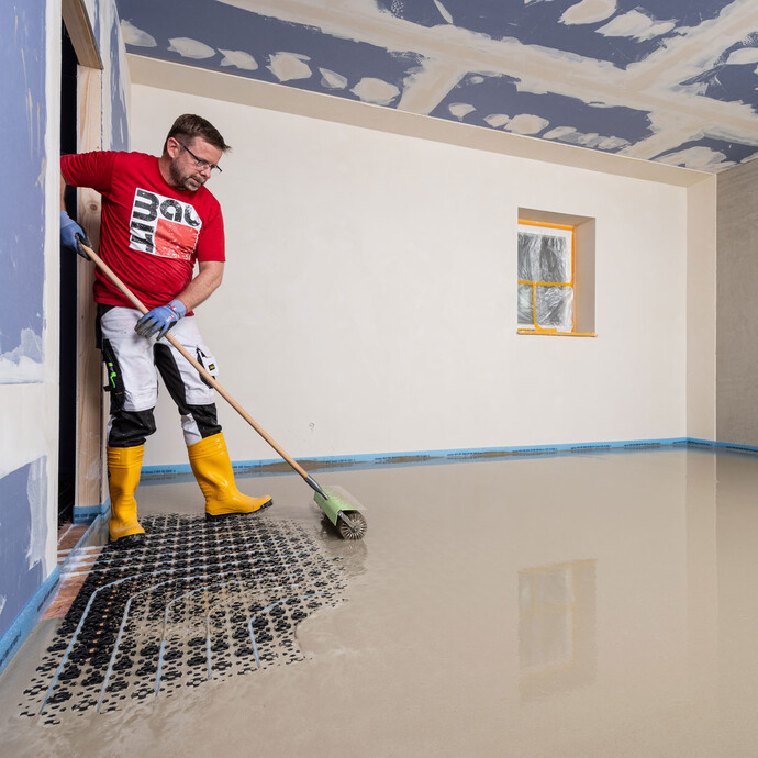 Le bricoleur purge la masse d'égalisation installée à l'aide d'un rouleau à pointes (également appelé rouleau hérisson).