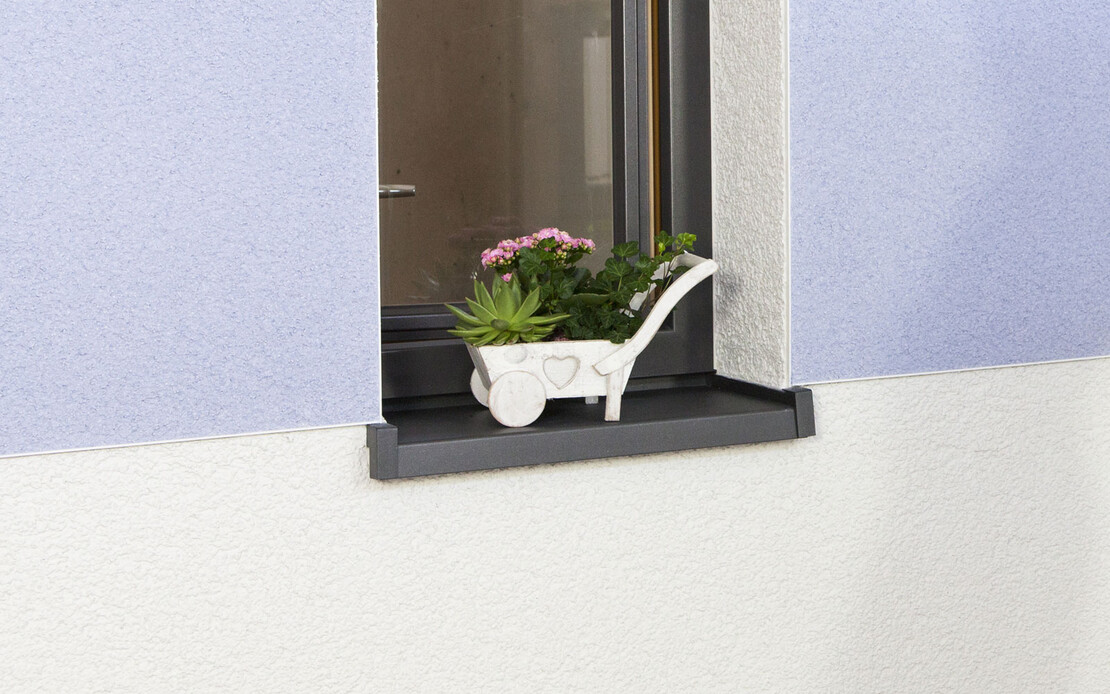Fassade mit zweifarbigem Oberputz in Wei&szlig; und Blau, sauber verarbeitet bis zur Fensterkante. Auf dem Fensterbrett steht eine kleine Pflanze.