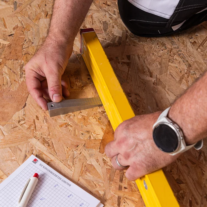 Photo de détail : les irrégularités du plancher en bois sont déterminées à l'aide d'une cale de mesure et d'un niveau à bulle. Les valeurs sont notées d'un coup d'œil avec Kulli.