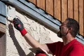 Mann verputzt Hausfassade mit Kelle und sieht dabei konzentriert aus. Heimwerkerarbeit an einer renovierungsbedürftigen Wand.