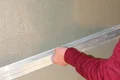 Person zieht mit einer Richtlatte Putz an einer Wand ab für ein glattes Finish beim Heimwerken.