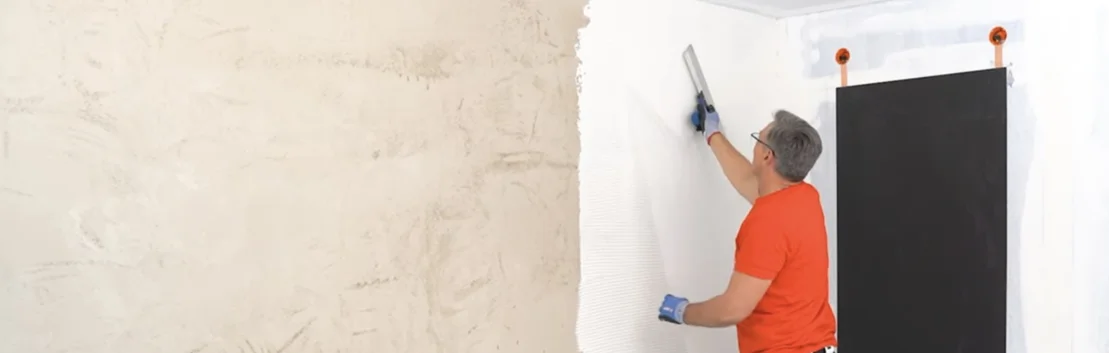 Heimwerker beim Spachteln einer Wand mit weisser Farbe; Schritt-für-Schritt-Erklärung für modernes Finish im Innenbereich.