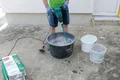 Le bricoleur mélange l'enduit fouetté de Munich avec de l'eau et un malaxeur électrique dans un seau à mortier.