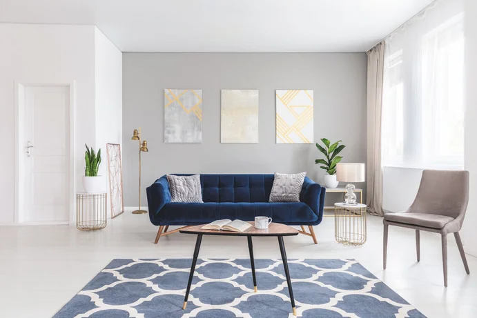 Moderner, heller Wohnraum mit blauer Couch, dekorativen Bildern und Teppich, ideal zur Inspiration für die Wohnraumgestaltung.