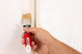 Hand streicht weiße Farbe mit Pinsel auf Wand, Heimwerkerprojekt für perfekte Wandgestaltung.