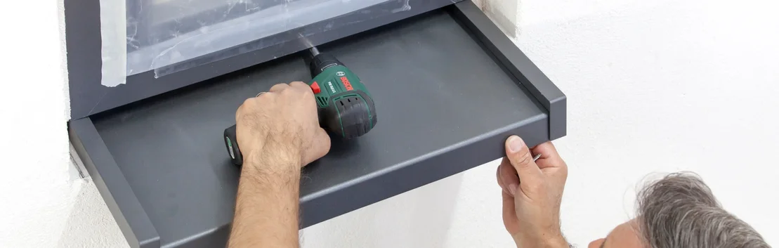 Un homme fixe une &eacute;tag&egrave;re au mur &agrave; l&rsquo;aide d&rsquo;une visseuse sans fil ; projet de bricolage avec des produits Baumit pour la maison.