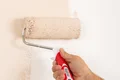 Hand streicht Wand mit Farbrolle in hellem Beige, ideal für Heimwerkerprojekte mit Baumit-Produkten.