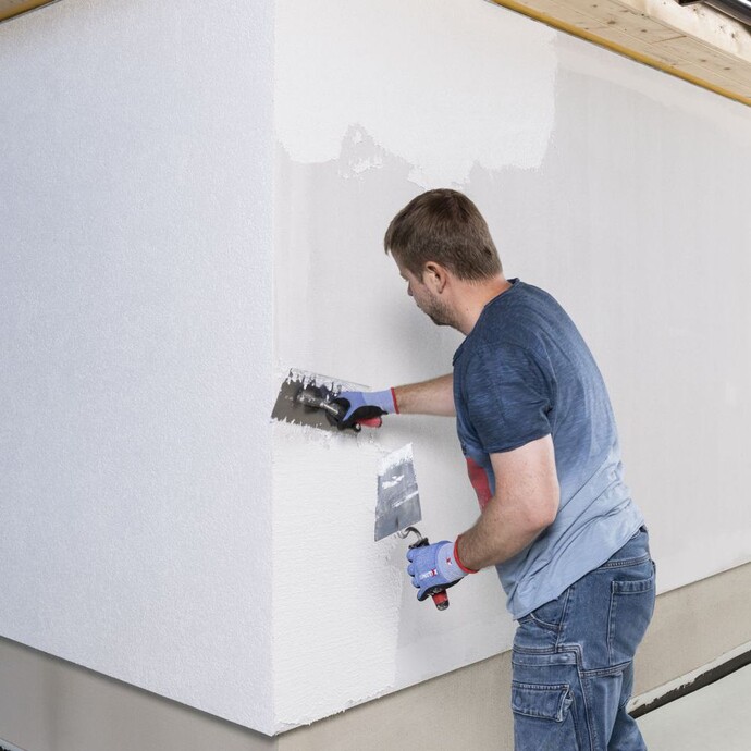 Mann trägt Strukturputz mit Glättkelle in Bahnen auf.