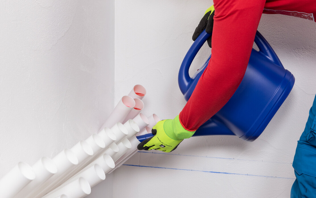 Person mit Schutzhandschuhen befüllt mit einer blauen Giesskanne Injektionstrichter in einer Wand zur Horizontalabdichtung.