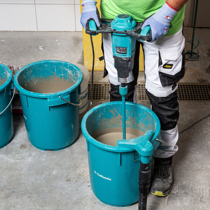 personne mélange la masse de nivellement dans le seau avec un mélangeur électrique.