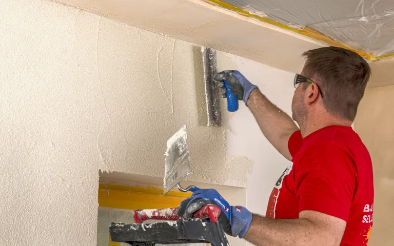 Heimwerker trägt Putz auf Wand auf; Schritt für Schritt zur perfekten Oberfläche mit Baumit Produkten.