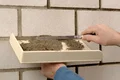 Mörtel auf Kelle vorbereiten, um Fugen einer Betonwand zu verfüllen; Anleitung für Heimwerkerprojekte mit Baumaterialien.
