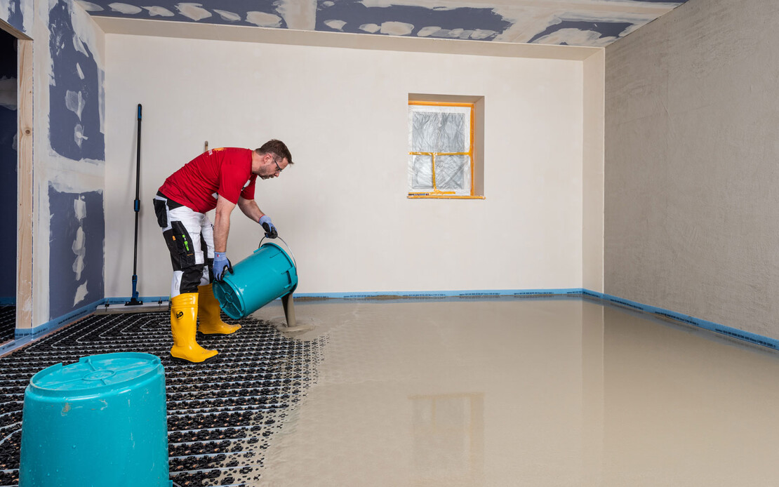 Heimwerker leert den Eimer mit Ausgleichsmasse auf die eingebaute Fu&szlig;bodenheizung.