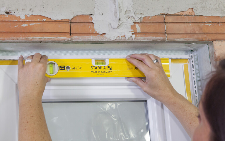 A l'aide d'un niveau à bulle, la femme vérifie si la moulure de la fenêtre est bien placée.
