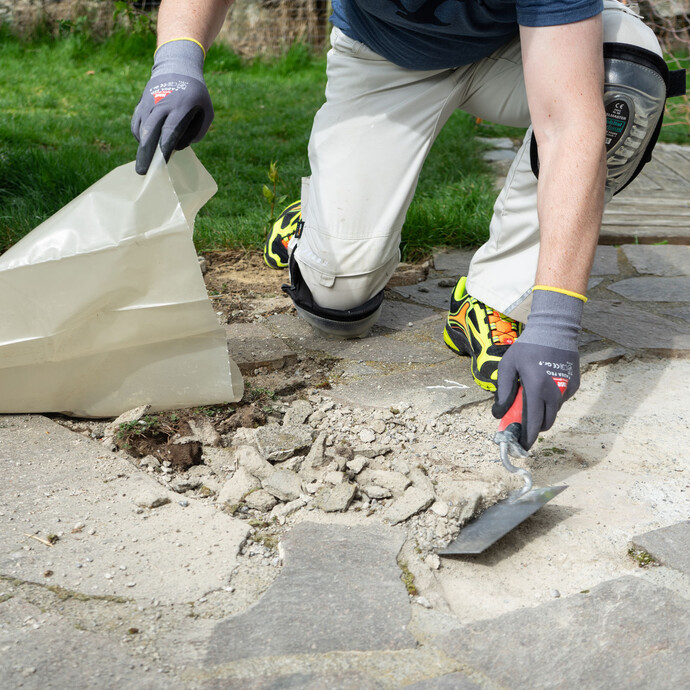 Person entfernt grobe Schmutz- und Mörtelreste mit einer Kelle von der freigelegten Fläche.