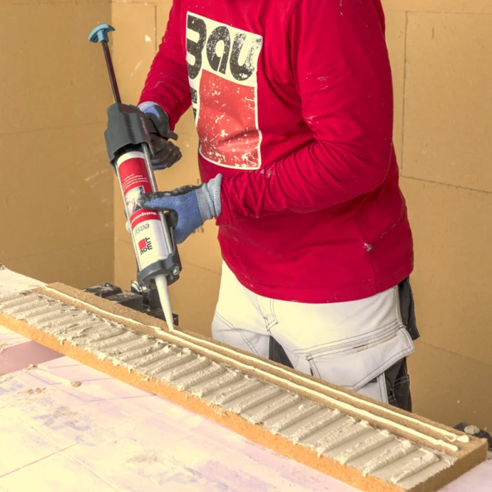 Un bricoleur applique de la colle à l'aide d'un pistolet à cartouche sur des panneaux isolants. Idéal pour une isolation efficace de la maison.