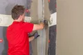 Heimwerker trägt Gewebe auf Fassadendämmung auf und glättet Spachtelmasse für eine professionelle Oberflächengestaltung.