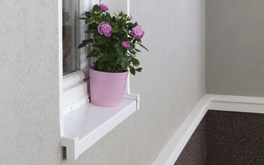 Eine Wand mit grauem Putz über und Mosaikputz unter weißen Stuckelementen. In der Wand ist ein Fenster, es steht ein Blumentopf auf dem Fensterbrett.