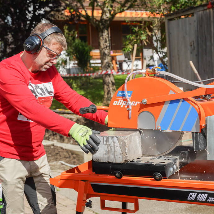 Heimwerker sägt Natursteine und schneidet Betonsteine im Garten mit der Norton Clipper Steinsäge, um eine Gartenmauer zu bauen.