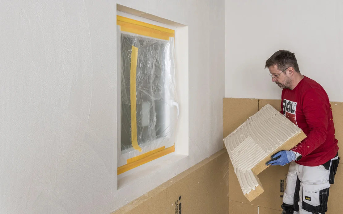 Heimwerker isoliert Wand mit D&auml;mmplatten; Fenster zum Schutz abgeklebt, Schritt-f&uuml;r-Schritt-D&auml;mmtechnik von Baumit.