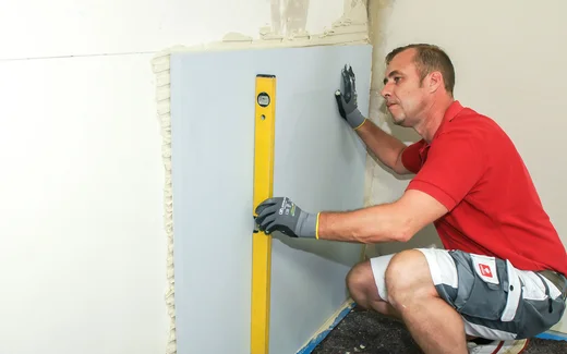 Person prüft die richtige Position der geklebten Kalziumsilikatplatte mit einer Wasserwaage.