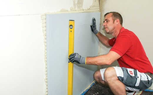 Person prüft die richtige Position der geklebten Kalziumsilikatplatte mit einer Wasserwaage.