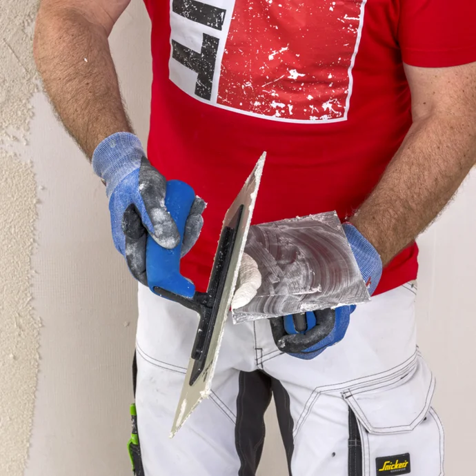 Heimwerker verspachtelt eine Wand mit Glättekelle und Putz; trägt rote Shirt mit Baumit-Logo.