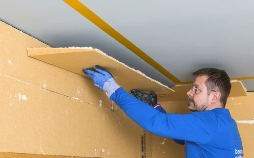 Mann montiert Deckenverkleidung mit Dämmplatten; zeigt Schritt zur DIY-Raumisolierung, geeignet für Heimwerkerprojekte.