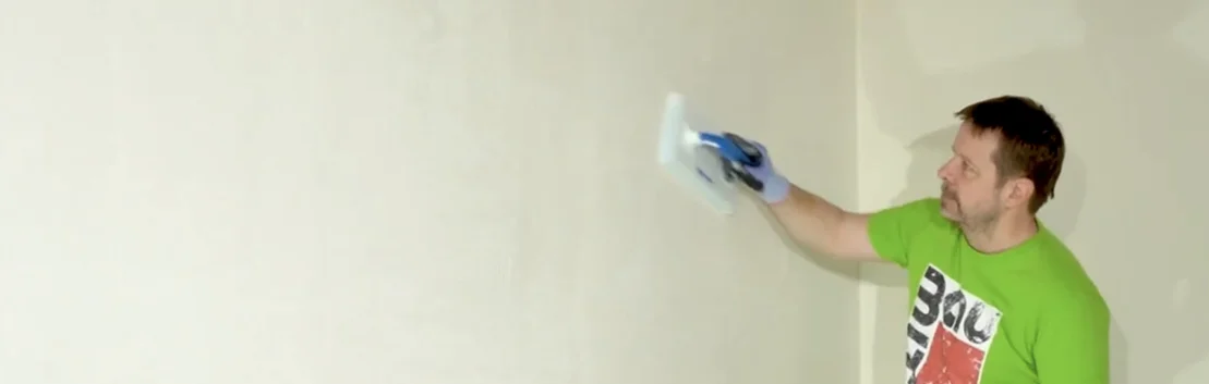 Mann glättet weisse Wand mit Spachtelmasse, DIY-Tipps für glatte Oberflächen.