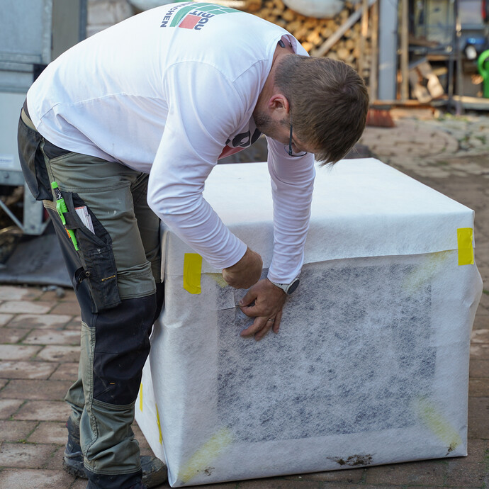 Heimwerker schneidet das Drainagevlies an der Sickerbox im Bereich der Rohrdurchführung mit einem Cuttermesser ein.