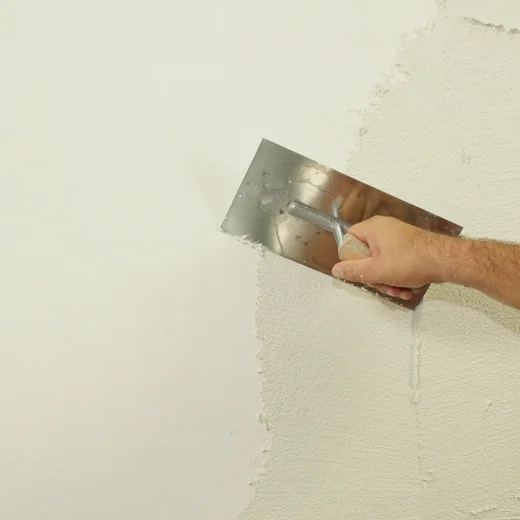 Hand verputzt eine Wand mit einer Kelle für gleichmäßige Oberflächenstruktur.