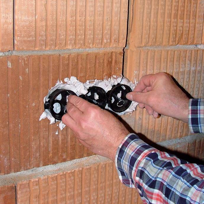 Die Leerdose für die Steckdose wird in den frisch aufgetragenen Gips im Rohbau eingesetzt.