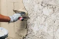 Hand trägt Putz auf Außenwand auf, nah, Schritt im Projekt zur Fassadensanierung, Anleitung für Heimwerker, Fokus auf Technik.