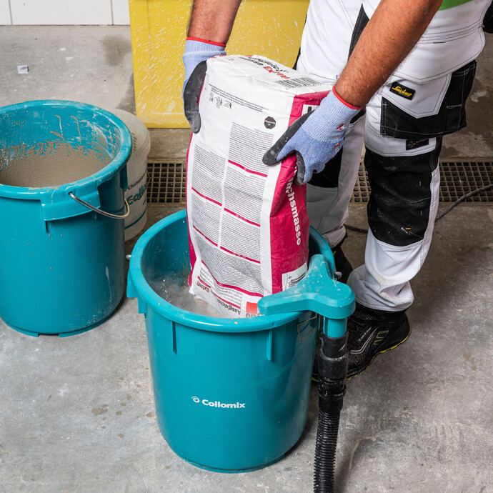 Photo de détail : une personne verse l'enduit d'égalisation Extrem de Baumit dans un seau bleu de Collomix, en portant des gants.