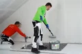 L'enduit au silicate Airless et au rouleau est appliqué par une personne à l'aide d'un rouleau, tandis qu'une autre personne lisse l'enduit.