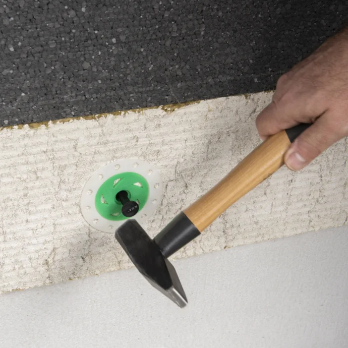 Pose d’un panneau isolant sur un mur à l’aide de chevilles pour isolant et d’un marteau. Étape de l’instruction pour l’isolation thermique.
