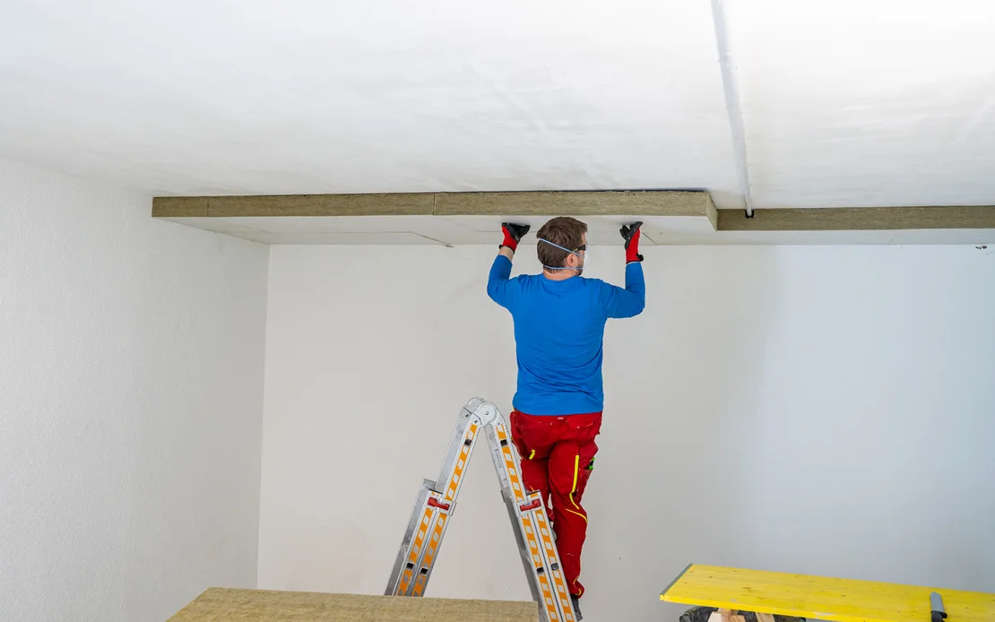 Heimwerker montiert Deckenverkleidung auf Leiter, Schritt-in-Schritt-Anleitung f&uuml;r DIY-Deckenrenovierung.