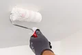 Un peintre applique une couche d’apprêt sur un plafond à l’aide d’un rouleau à peinture ; instructions étape par étape destinées aux bricoleurs pour la rénovation d’un plafond.