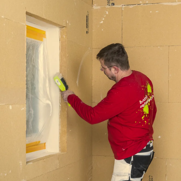 Un bricoleur enduit une cloison en plaques de plâtre avec du papier de verre dans le cadre de travaux d'aménagement intérieur.
