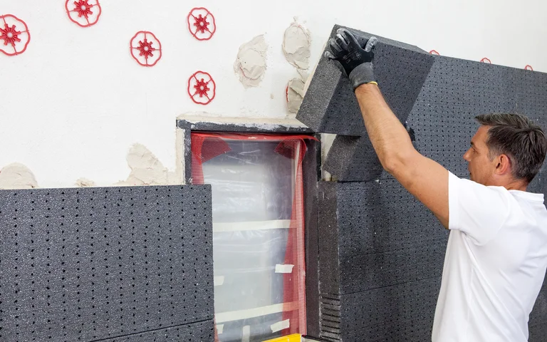 Un bricoleur pose des panneaux isolants sur une façade afin d’améliorer l’efficacité énergétique. Instructions étape par étape sur le site web de Baumit.