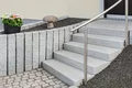 Moderne Eingangstreppe mit Edelstahlgeländer, umgeben von Steinelementen und Blumenarrangement, ideal für Heimwerkerprojekte.