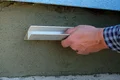 Eine Hand verputzt eine Wand mit einem Flächenspachtel, um eine glatte Oberfläche zu schaffen.
