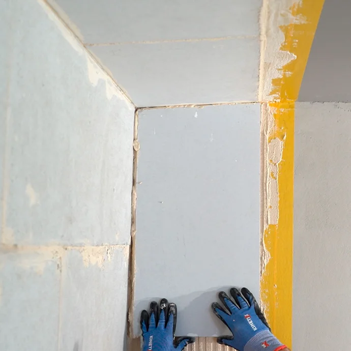 Heimwerker setzt den Kalziumsilikatplatte Anschlusskeil vorsichtig in den frisch aufgetrgenen Putz. Der Keil stösst bündig an die geklebte Platte an der Wand und Decke.