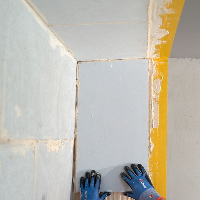 Heimwerker setzt den Kalziumsilikatplatte Anschlusskeil vorsichtig in den frisch aufgetrgenen Putz. Der Keil stösst bündig an die geklebte Platte an der Wand und Decke.