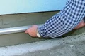 Hand richtet Putzschicht mit Aluminium-Abziehlatte an einer Hauswand aus, ideal für Heimwerkerprojekte.