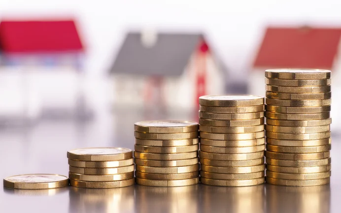 Gestapelte Münzen vor unscharfen Modellhäusern symbolisieren Investitionen in Renovierung und Wertsteigerung von Immobilien.