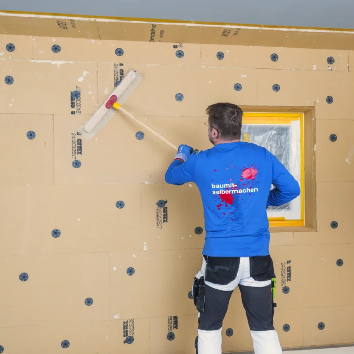 Heimwerker montiert Fassadendämmung mit Baumit-Produkten, Fensterbereich wird präzise bearbeitet.