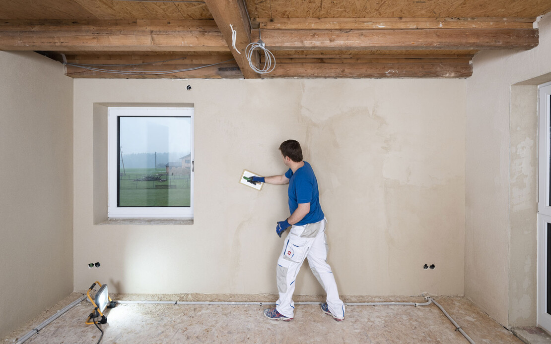 Heimwerker filzt den aufgetragenen Kalkputz im Streiflicht.